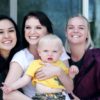 woman carrying baby with two ladies beside her smiling